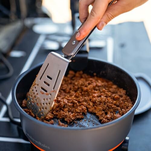 Person stirring ground beef in a pan with a spatula