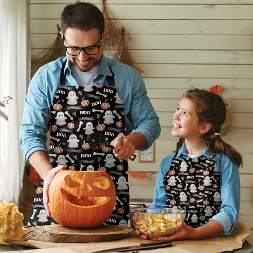 Father and daughter carving a pumpkin together while wearing matching Halloween aprons.