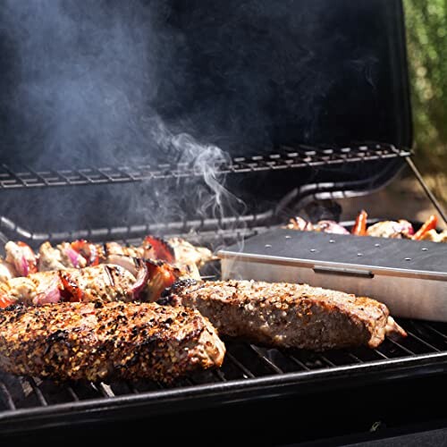 Steak and vegetables grilling with smoke box on barbecue.