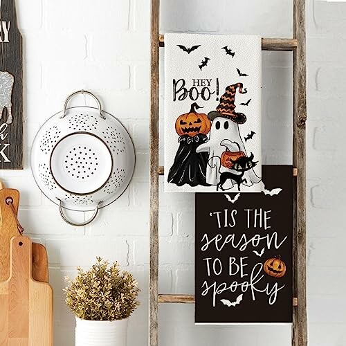 Halloween-themed kitchen towels with ghost and pumpkin designs on a wooden ladder.
