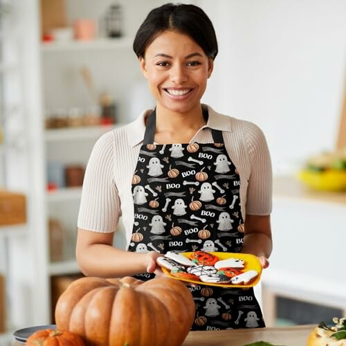 Person wearing Halloween apron holding decorated cookies