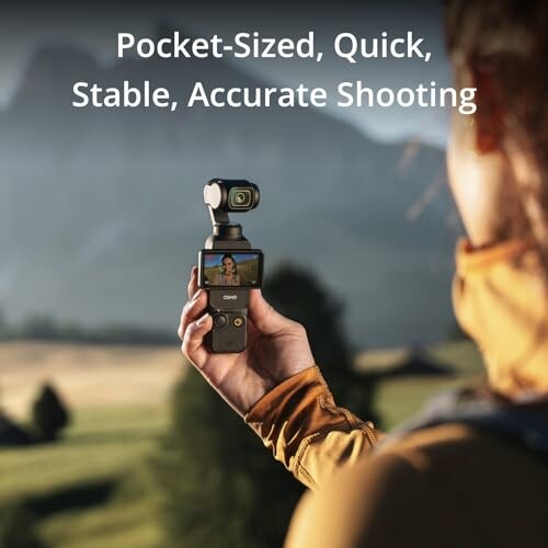 Person holding a handheld camera gimbal with a landscape in the background.