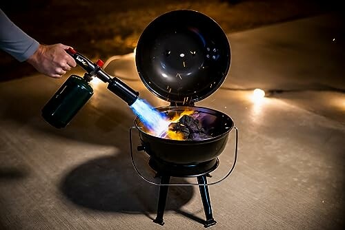 Person lighting portable grill with a torch on a patio.