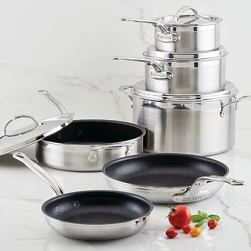 Stainless steel cookware set with pots and pans on a marble surface.