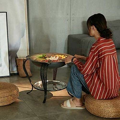 Woman sitting on a cushion beside a round grill table indoors.