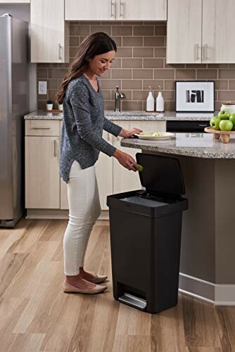 Woman using a black kitchen trash can with a foot pedal.